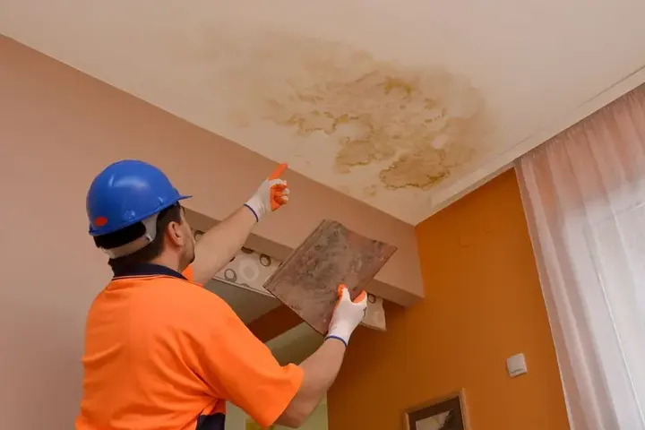 Technician inspecting a water-stained ceiling below a leak in Manchester