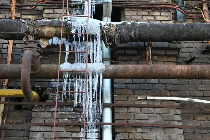 Ice hanging from frozen pipes along a brick basement wall in winter