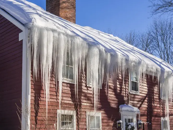 Ice dam and icicles along the eaves of a snow-covered Manchester house