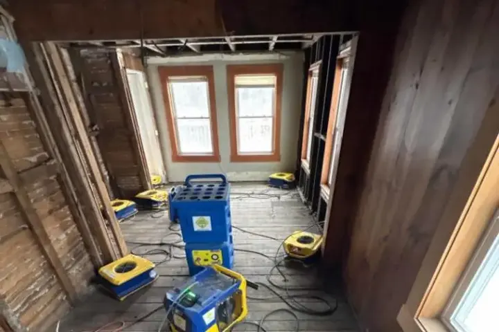 Air movers and dehumidifiers drying an opened-up room with wood framing